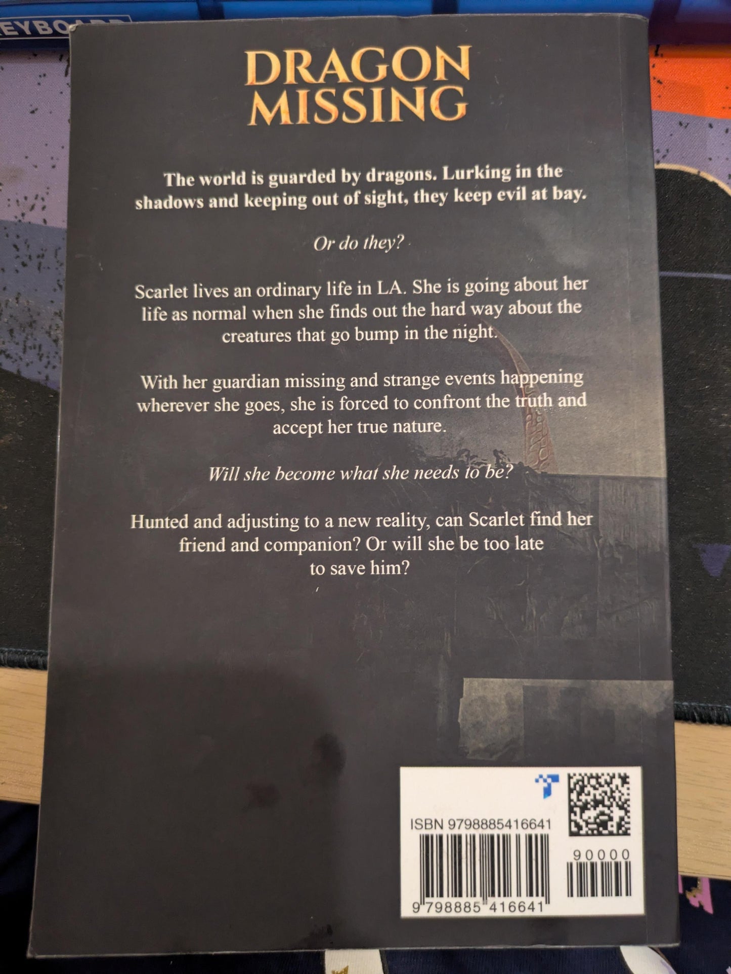 The back cover of the book 'Dragon Missing' by Talia Becket featuring a dark gray background with gold and white text, a barcode, and a QR code.