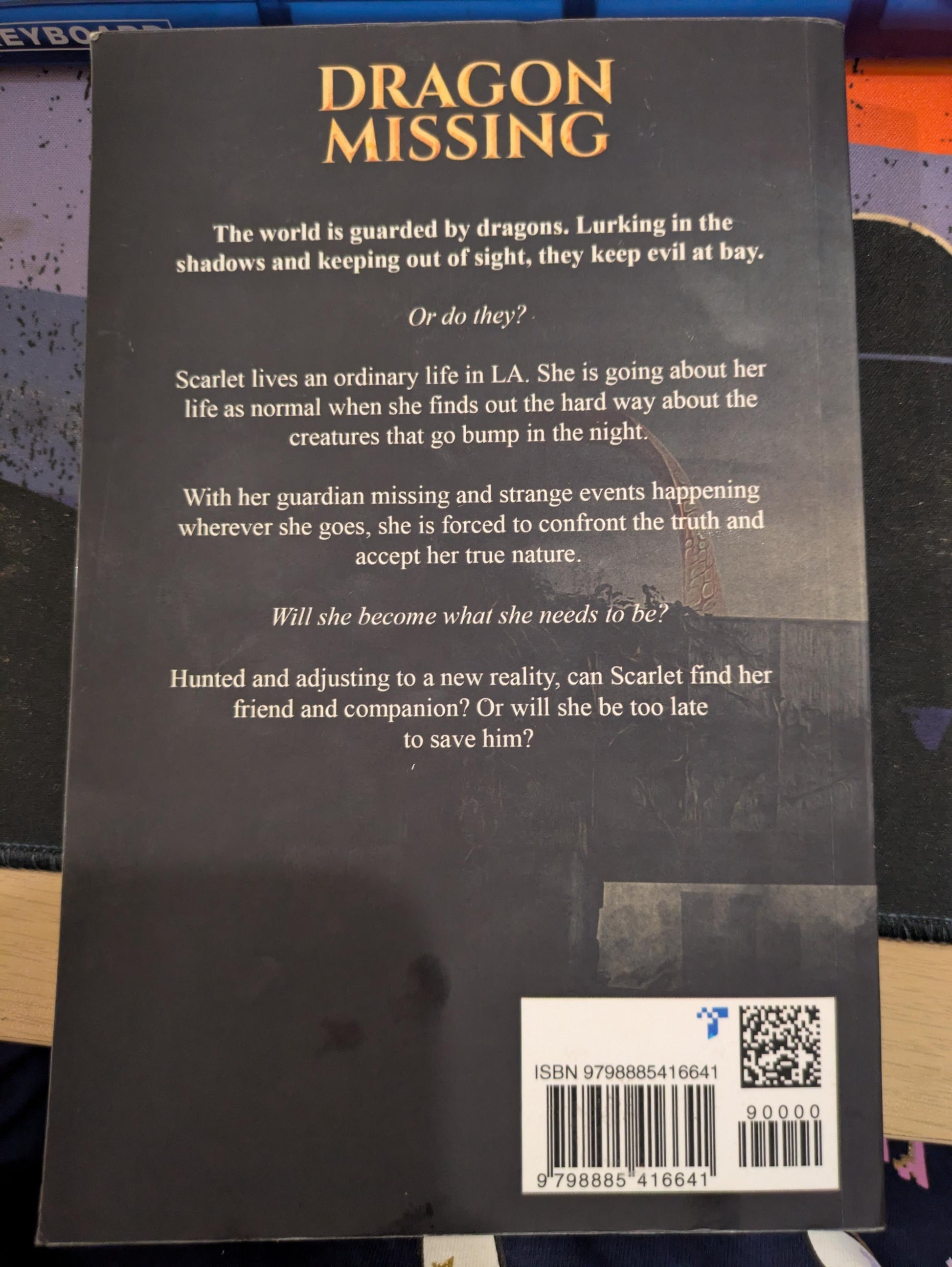 The back cover of the book 'Dragon Missing' by Talia Becket featuring a dark gray background with gold and white text, a barcode, and a QR code.
